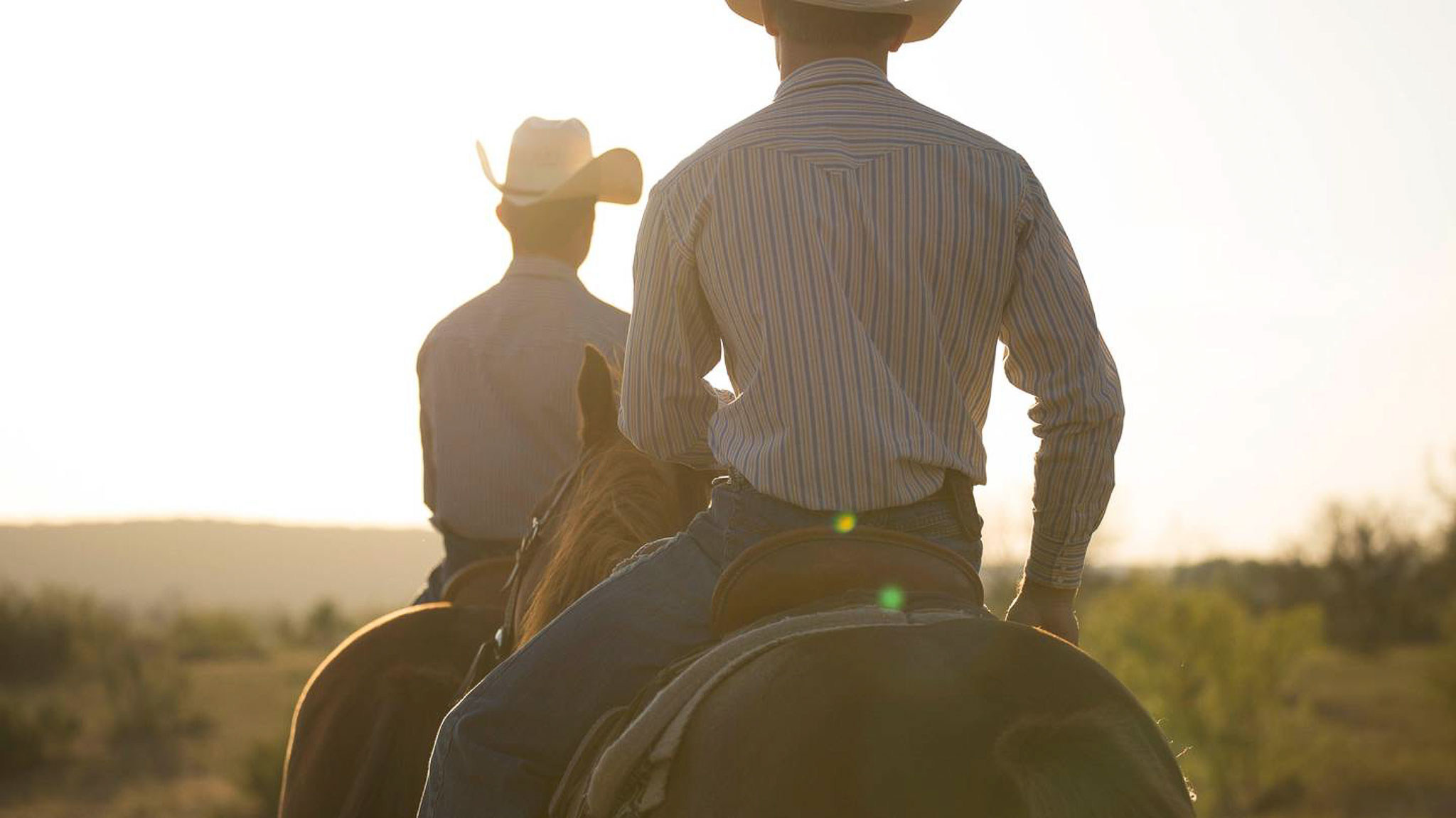 A couple ride horses at sunset at Wildcatter Ranch.