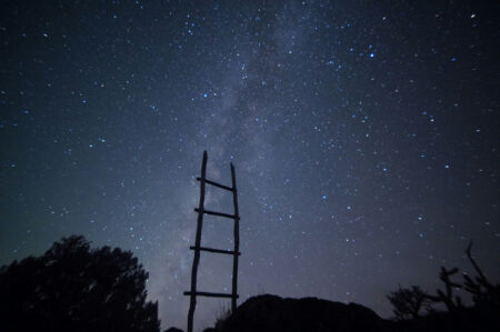 A ladder reaches to the sky on a starry night.
