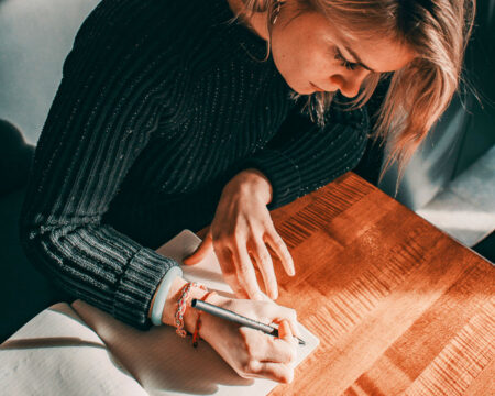 A woman hunched over a desk is working hard on her writing project.