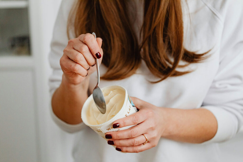 A woman dips her spoon into a tub of ice-cream.