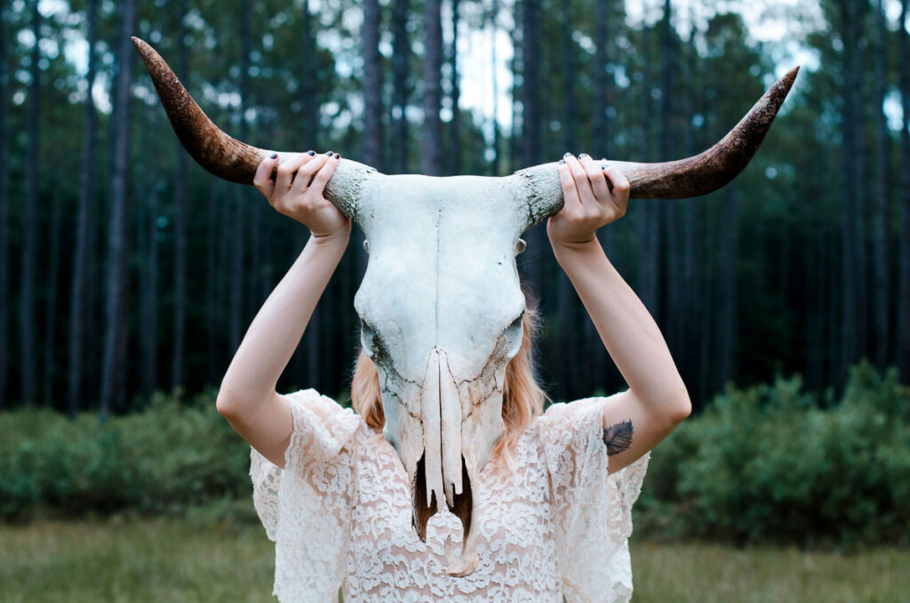 A ghostly woman uses a cow's skull to mask her face. 