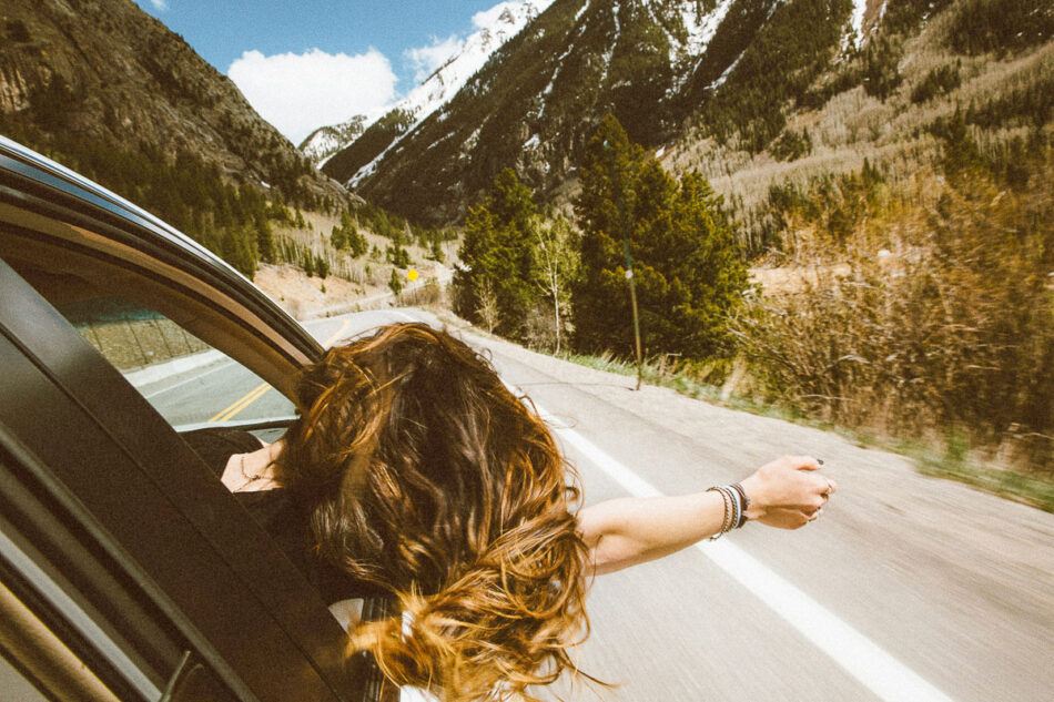 A woman leans out of an open car window on a road trip.