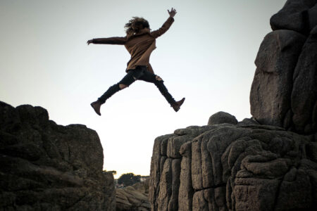 A woman leaps between two boulders.