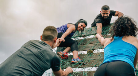 Participants in an obstacle course help each other over a barrier.