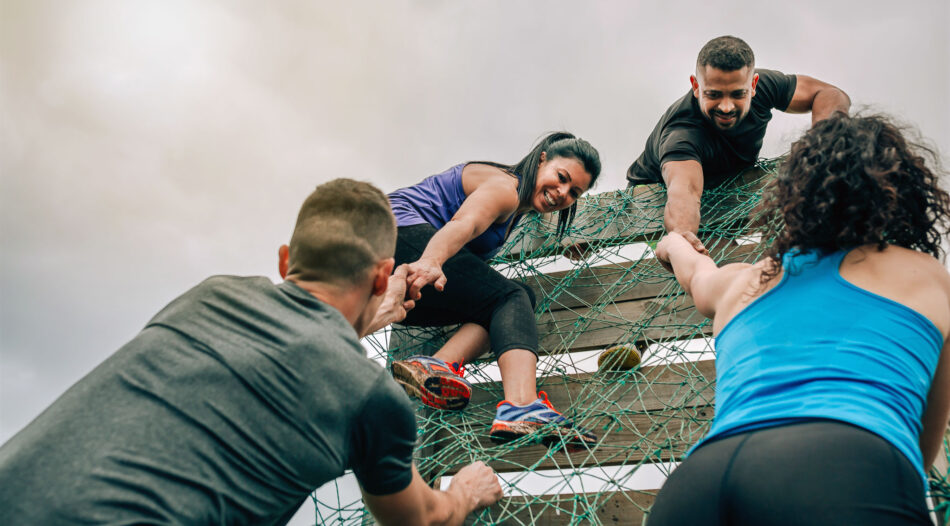Participants in an obstacle course help each other over a barrier.